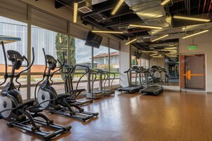 Un gimnasio con diversas máquinas de cardio, ventanas amplias y suelo de madera.