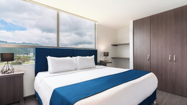 Een moderne hotelkamer met een groot bed, een kledingkast, een nachtkastje en uitzicht op het omliggende landschap.