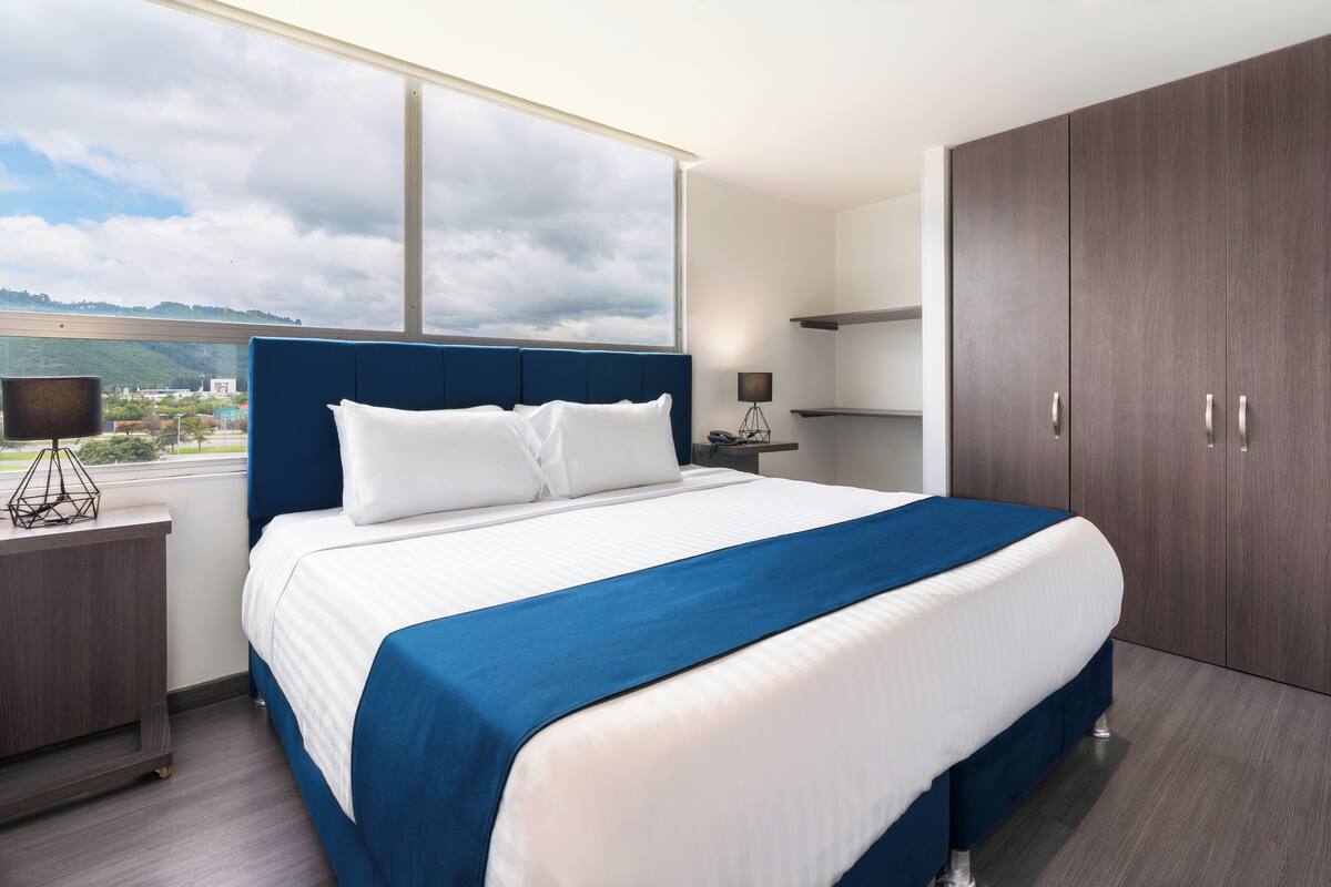 Ein modernes Hotelzimmer mit einem großen Bett, einem Kleiderschrank, einem Nachttisch und Blick ins Freie.