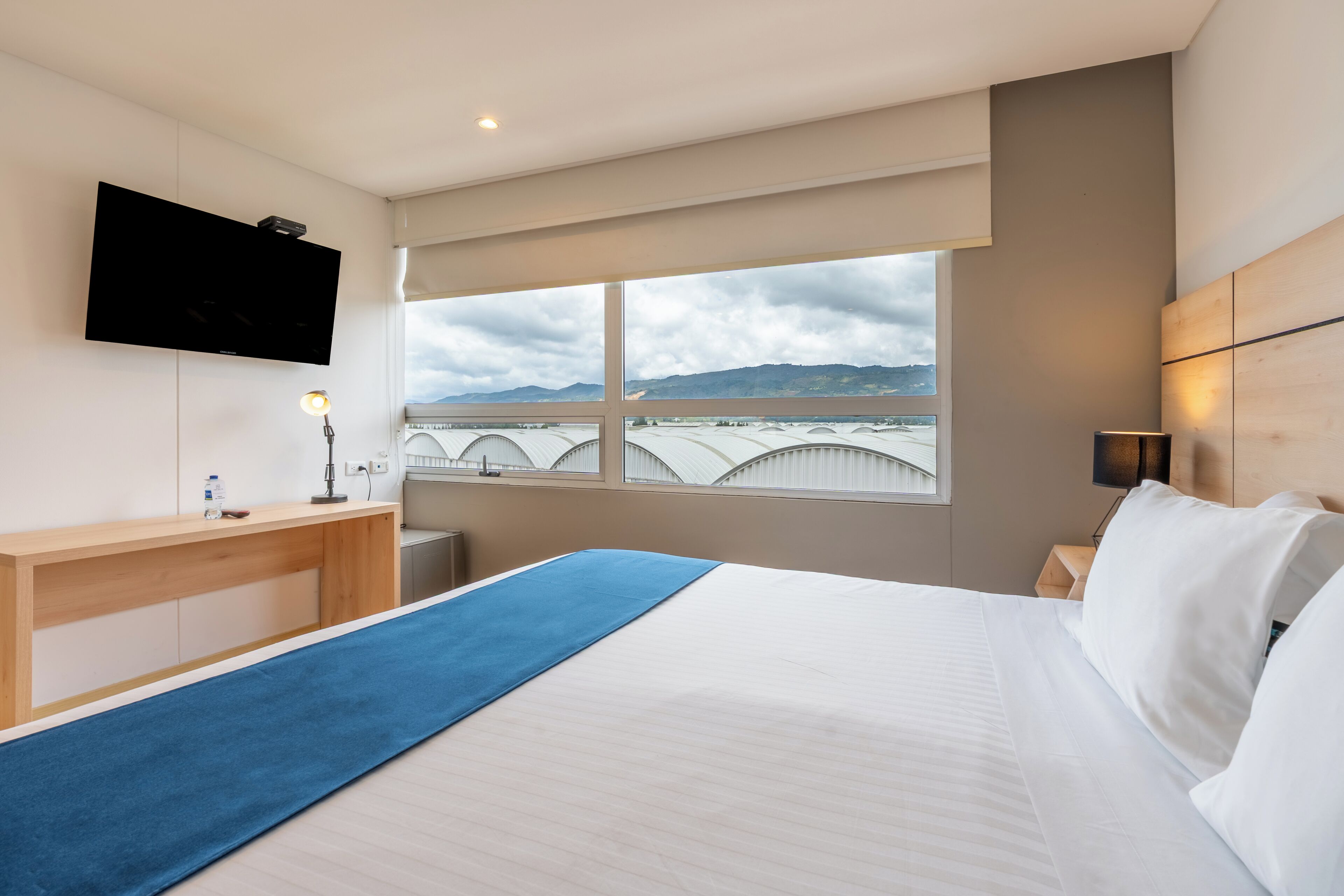 A hotel room with a bed, a desk, a TV, and a window with a view of a bridge and mountains.