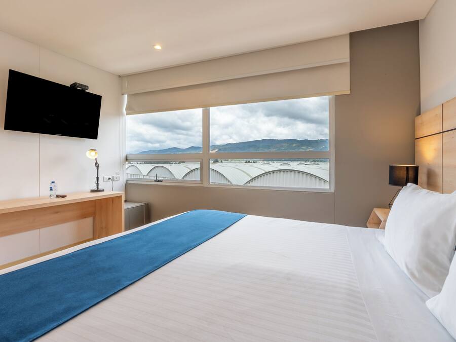 A hotel room with a bed, a desk, a TV, and a window with a view of a bridge and mountains.