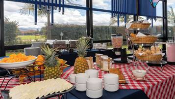 Montaje de bufé con diversos alimentos y utensilios sobre una mesa, con una vista panorámica a través de amplios ventanales.