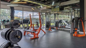 Een fitnessruimte met gewichthefapparatuur, banken en uitzicht op groen buiten.