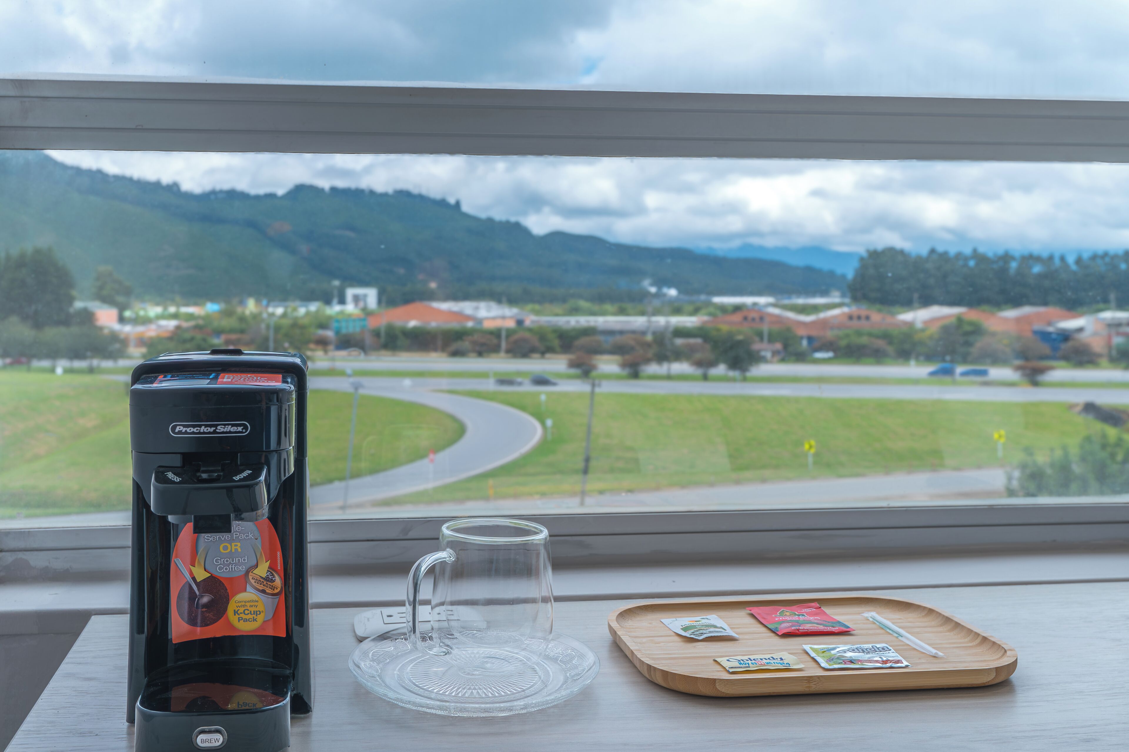 A coffee maker on a table with a view of a road and buildings in the background.