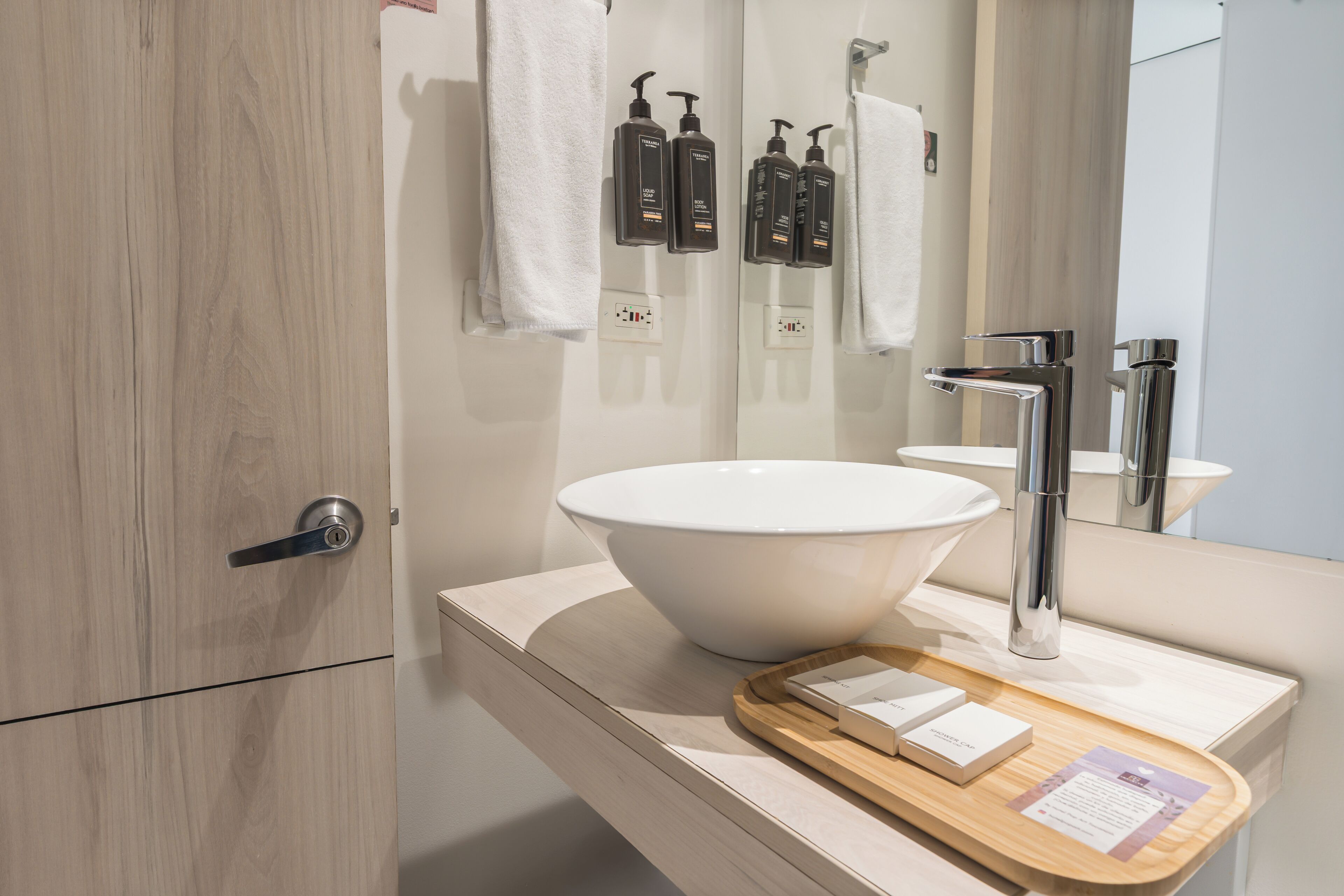 Un baño moderno con un lavabo grande de color blanco, un grifo cromado y una bandeja de madera con artículos de aseo.