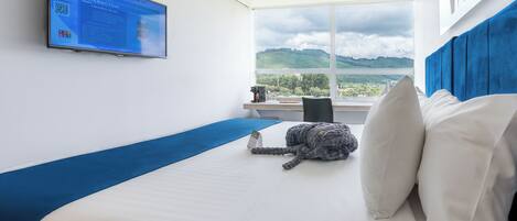 Habitación de hotel con cama, televisión montada en la pared, ventana con vista a las montañas y una pared de acento azul.