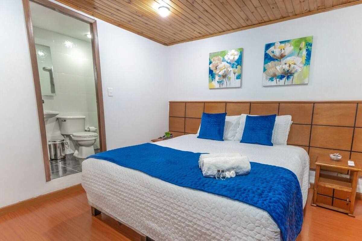 Un dormitorio con una cama, una mesita de noche, techo de madera y dos cuadros en la pared.