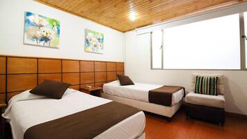 A hotel room with two beds, wooden headboard, artwork on the wall, and a window with blinds.