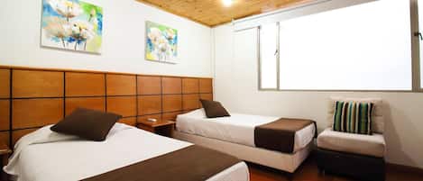 A hotel room with two beds, wooden headboard, artwork on the wall, and a window with blinds.