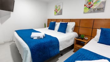 A hotel room with two beds, each with blue and white bedding, a wooden headboard, a small bedside table with a plant, and a wall-mounted TV.