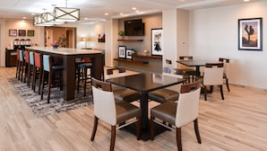 A modern hotel dining area with a central island, bar stools, and a long dining table. - Hampton Inn El Centro (El Centro)