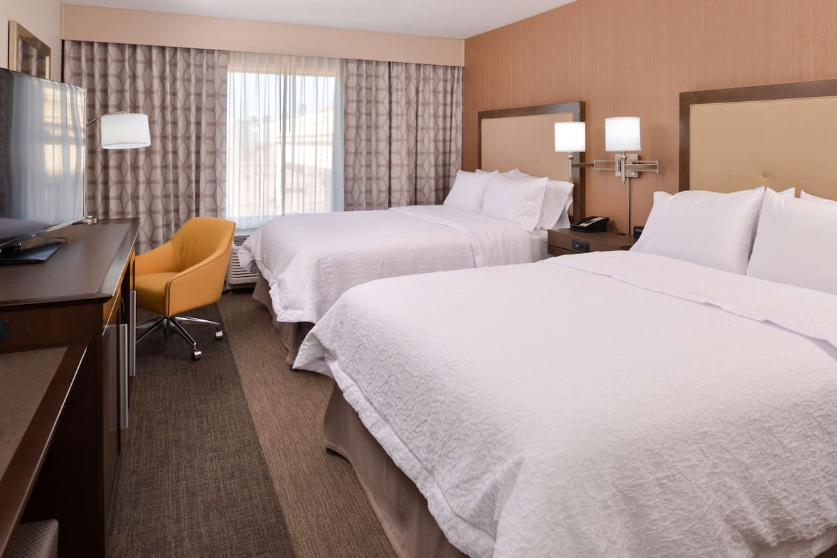 A hotel room with two beds, a desk, a chair, and a TV.