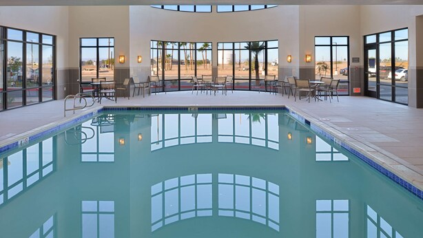 An indoor swimming pool with clear views of the parking lot and palm trees outside.