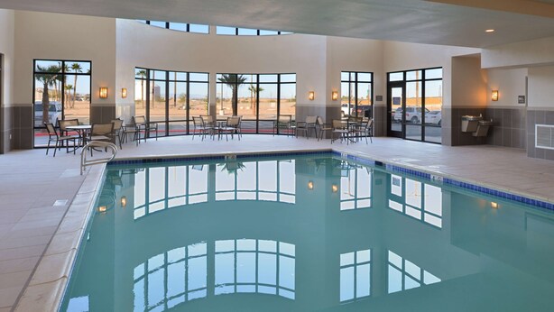 An indoor swimming pool with clear views of palm trees and a parking lot through large windows. - Hampton Inn El Centro (El Centro)