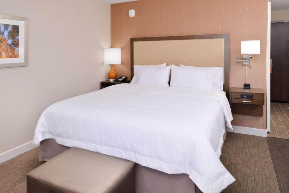 A hotel room with a large bed, a bedside table with a lamp, a small table with a phone, and a wall-mounted light.