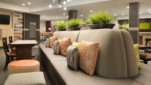 A modern hotel lobby with a long bench, potted plants, and a digital screen. - Home2 Suites by Hilton Houston Webster (Webster)