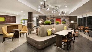A modern lounge area with a sofa, chairs, a dining table, and a bar counter. - Home2 Suites by Hilton Houston Webster (Webster)