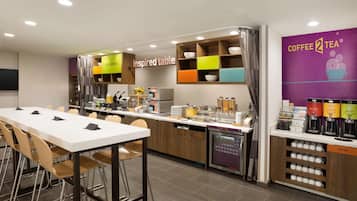 A modern coffee shop with a long communal table, a coffee bar, and a variety of coffee machines and beverages.