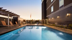 A swimming pool with lounge chairs and a pergola, surrounded by a fence and a building with exterior lighting. - Home2 Suites by Hilton Houston Webster (Webster)