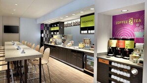 A modern kitchen area with a long counter, bar stools, and a coffee station with labeled dispensers. - Home2 Suites by Hilton Cleveland Independence (Independence)