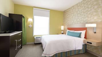 A hotel room with a bed, a television, a desk, and a window with curtains.
