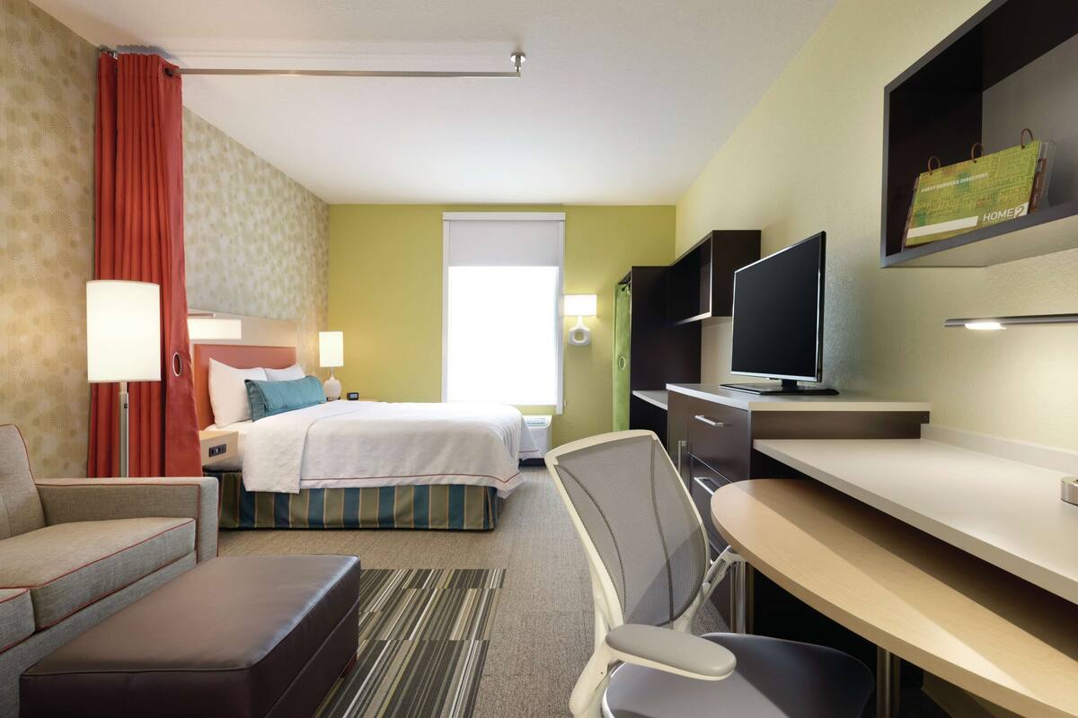 A hotel room with a bed, a desk, a chair, a television, and a window with curtains.