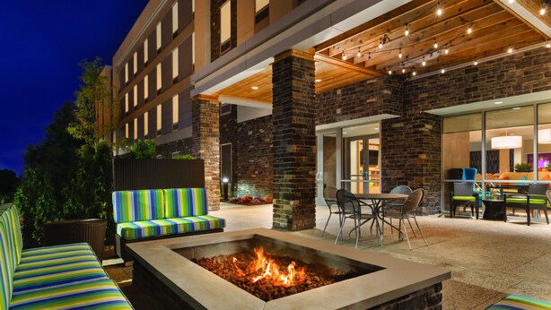 An outdoor seating area with a fire pit, cushioned seating, and a covered patio with tables and chairs. - Home2 Suites by Hilton Cleveland Independence (Independence)