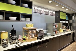 Una barra de desayuno con máquina para gofres, cafetera y diferentes condimentos.