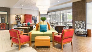 A modern lobby with a green sofa, red chairs, a wooden table, and a large window offering a view of the outside. - Home2 Suites by Hilton Cleveland Independence (Independence)