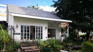 A white cottage with a tiled roof, large windows, and a welcoming sign. - The Goodville Cottage (Pak Chong)