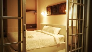 A bedroom with a bed, a nightstand, and a wall-mounted light fixture. - The Goodville Cottage (Pak Chong)