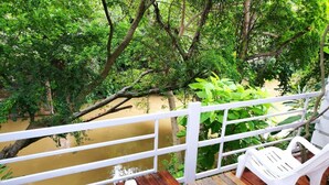 A wooden deck with white plastic chairs and a bench overlooking a river. - The Goodville Cottage (Pak Chong)