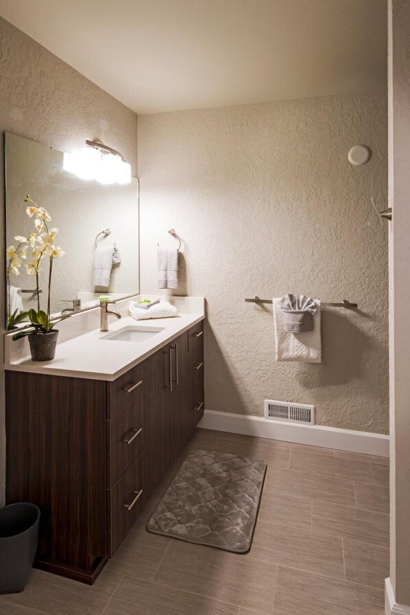 Une salle de bain moderne avec un meuble-lavabo en bois, un grand miroir, une orchidée en pot, un porte-serviettes et un espace douche.