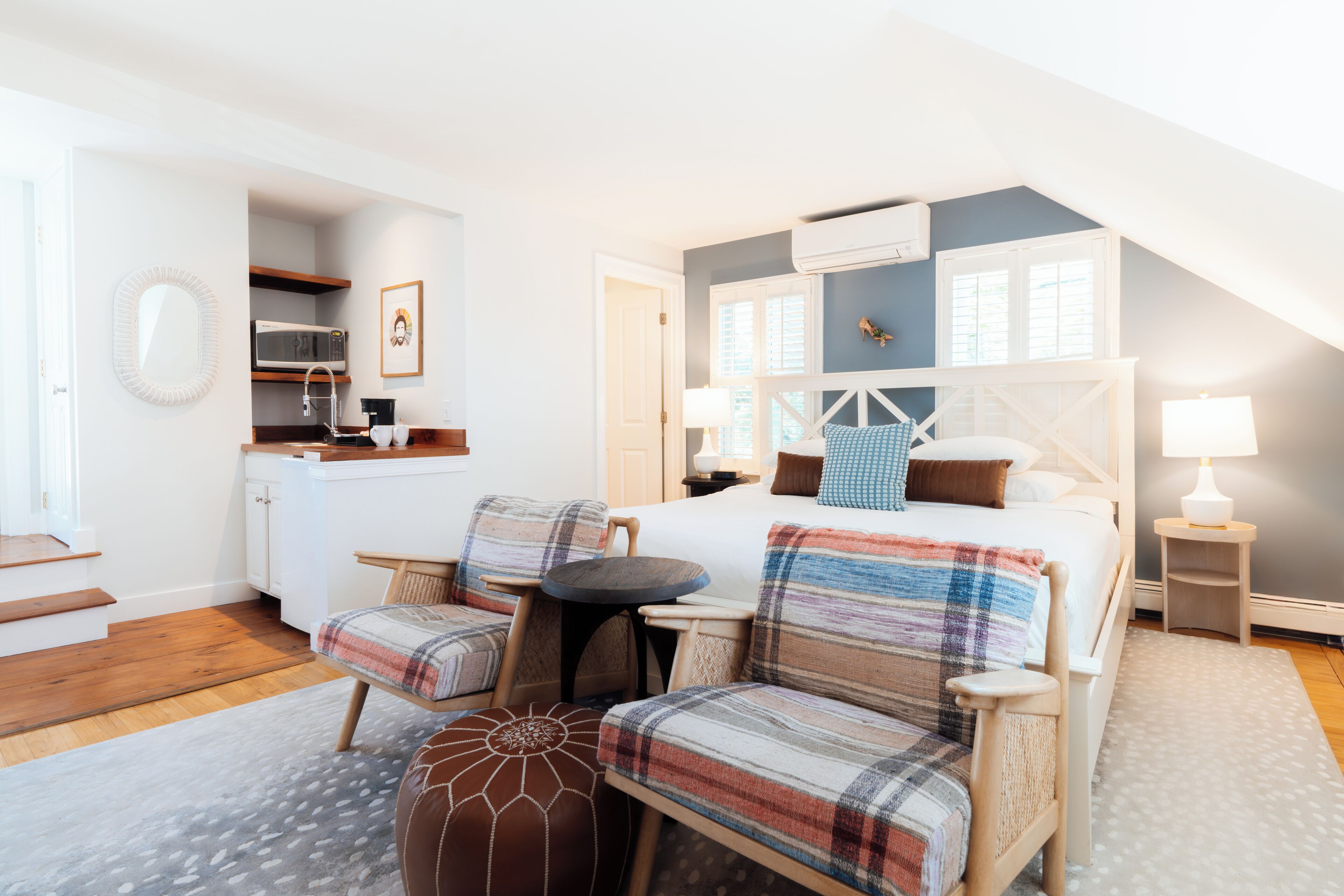 A cozy bedroom with a bed, two chairs, a small table, and a kitchenette.