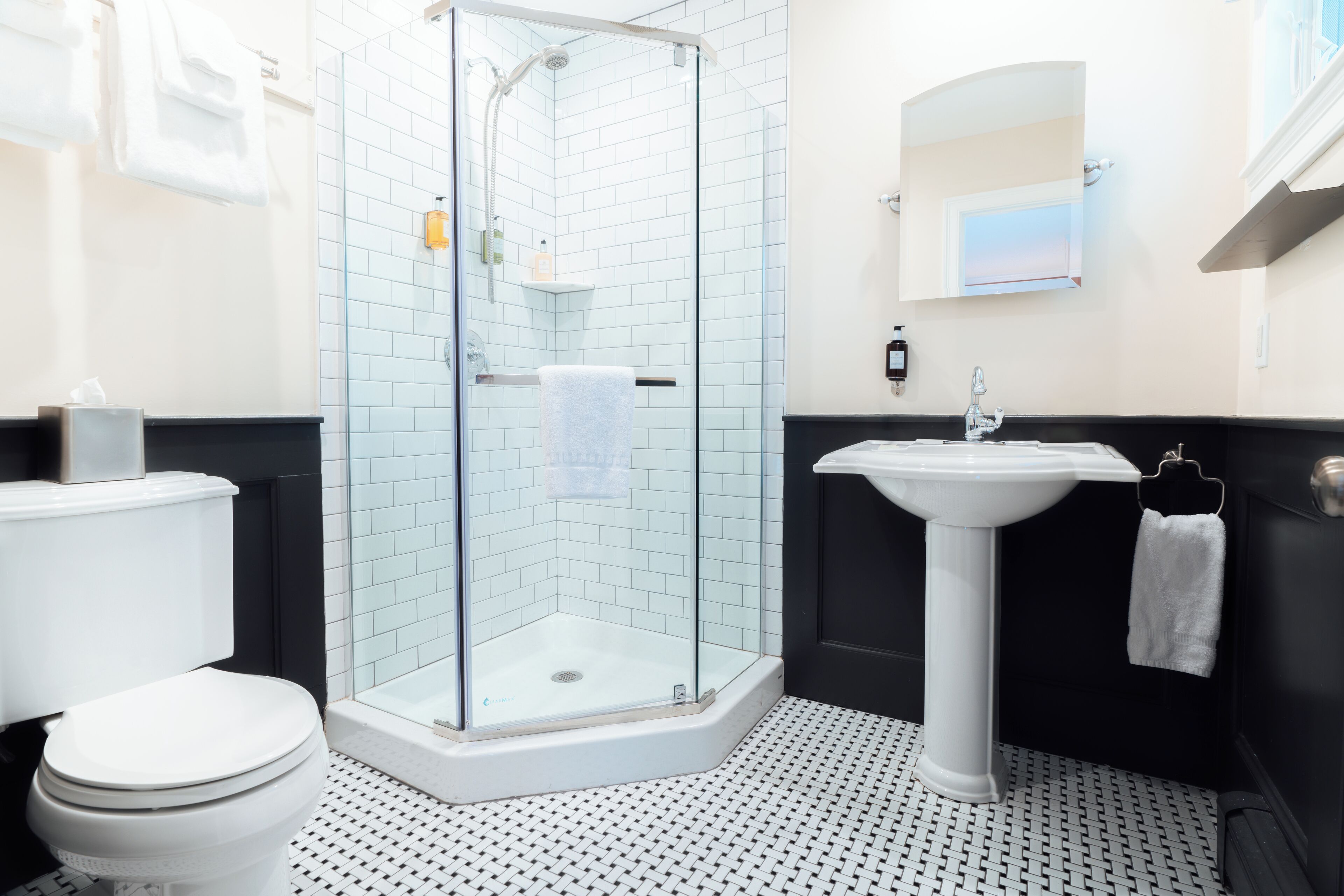 A bathroom with a glass shower enclosure, a white toilet, a pedestal sink, and a black vanity.