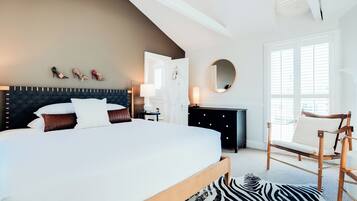 Een moderne slaapkamer met een groot bed, een houten hoofdbord, een zwart-wit kleed, een houten stoel en een spiegel aan de muur.