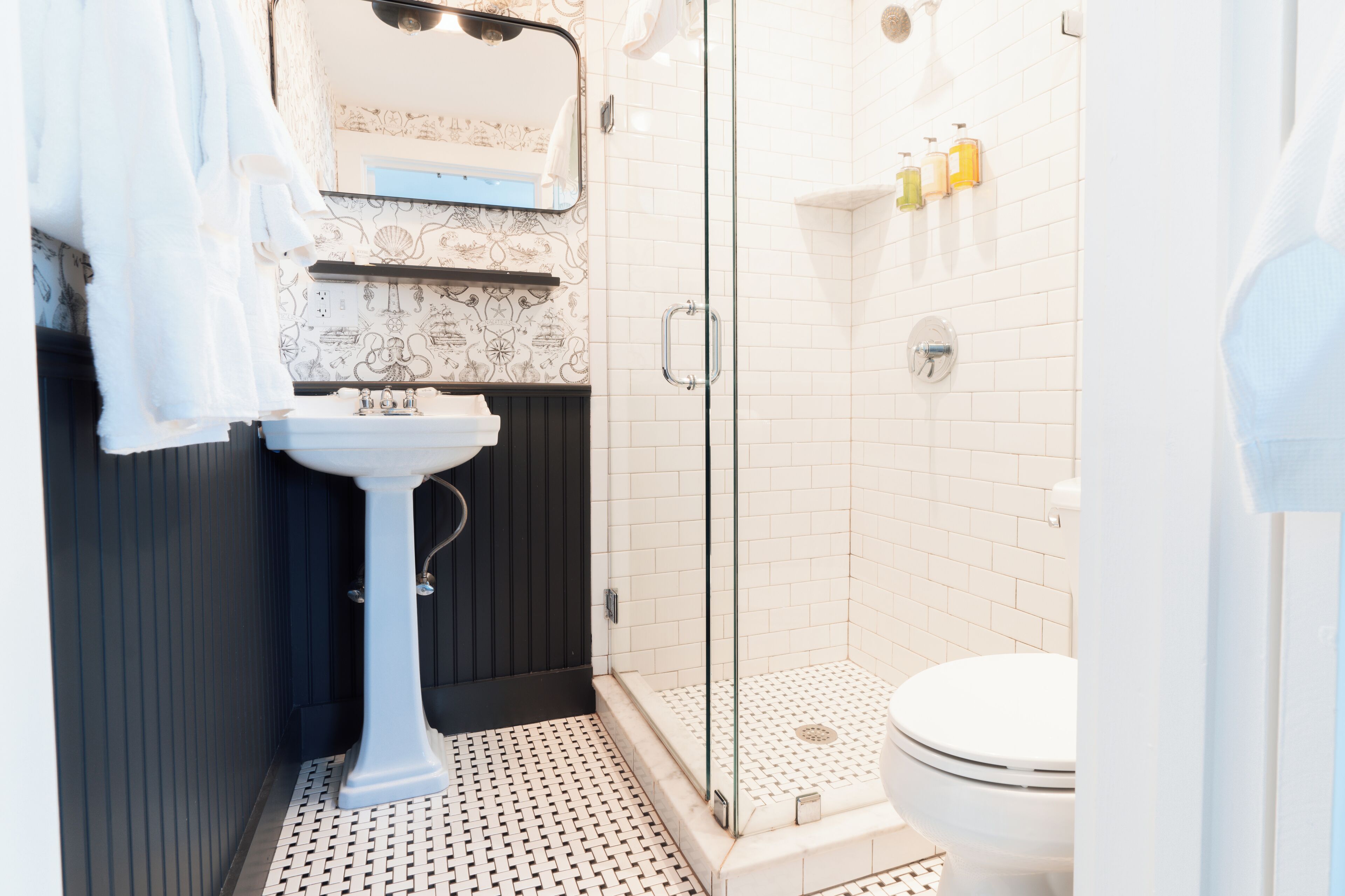 A bathroom with a white sink, dark wooden paneling, a glass shower enclosure, and a white toilet.