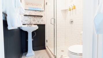 A bathroom with a white sink, dark wooden paneling, a glass shower enclosure, and a white toilet.