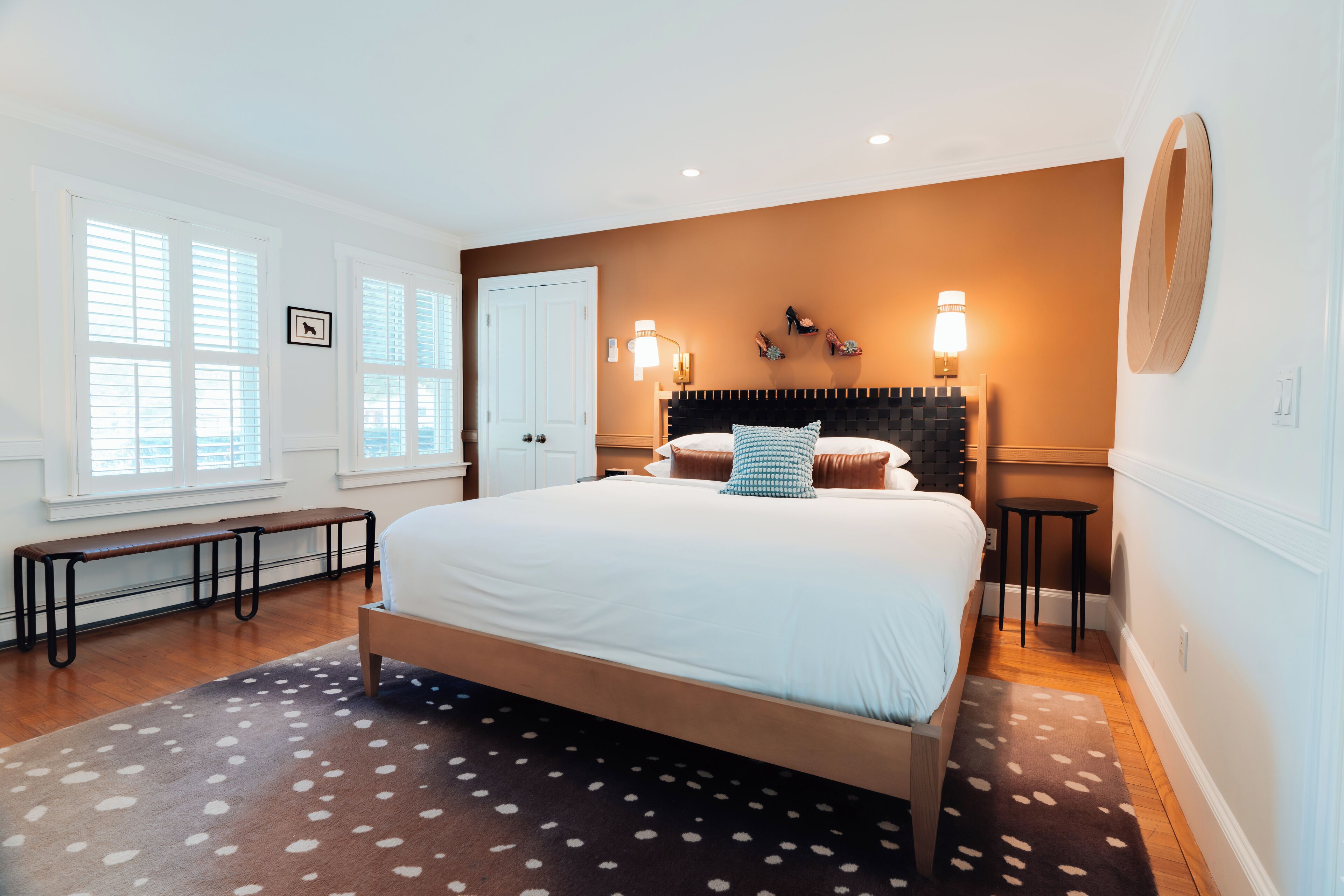 A bedroom with a large bed, a bench, a small table, and a wall-mounted mirror.