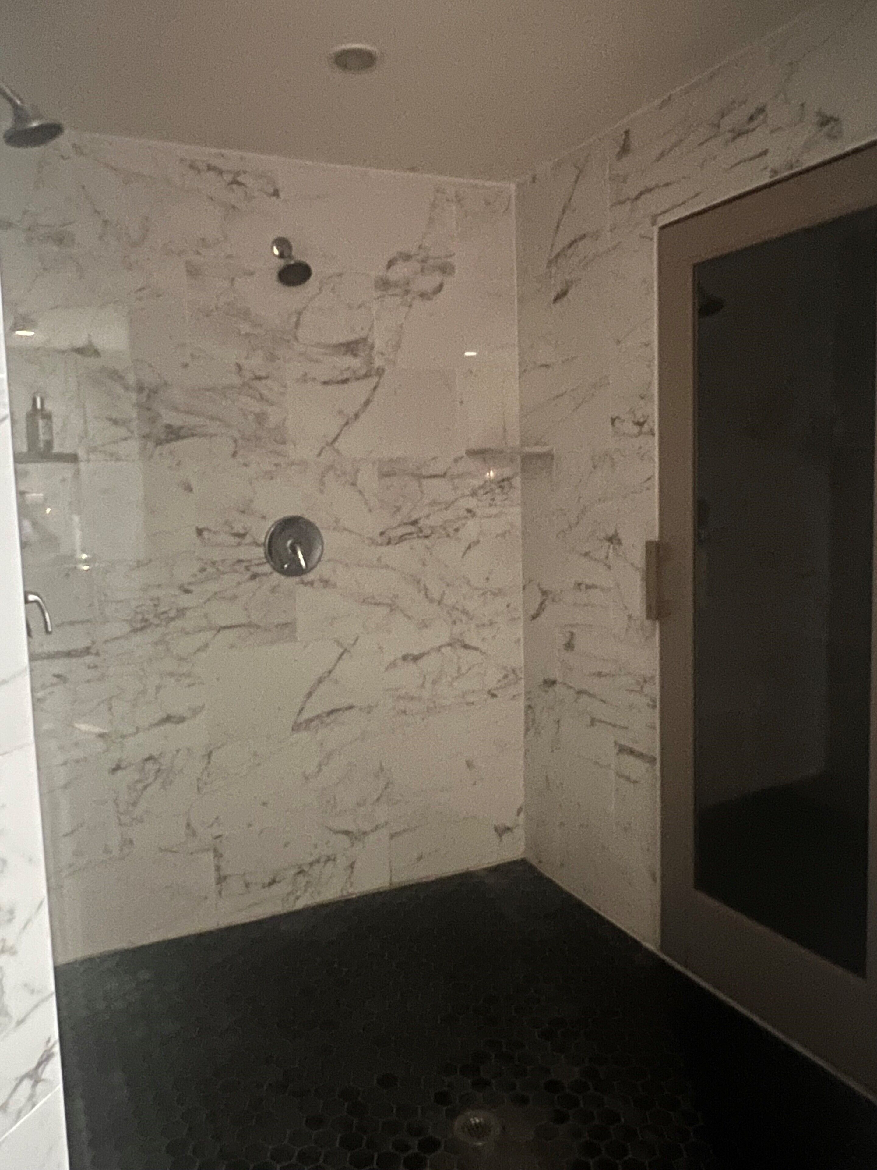 A modern bathroom with a glass shower enclosure, marble walls, and a black tiled floor.