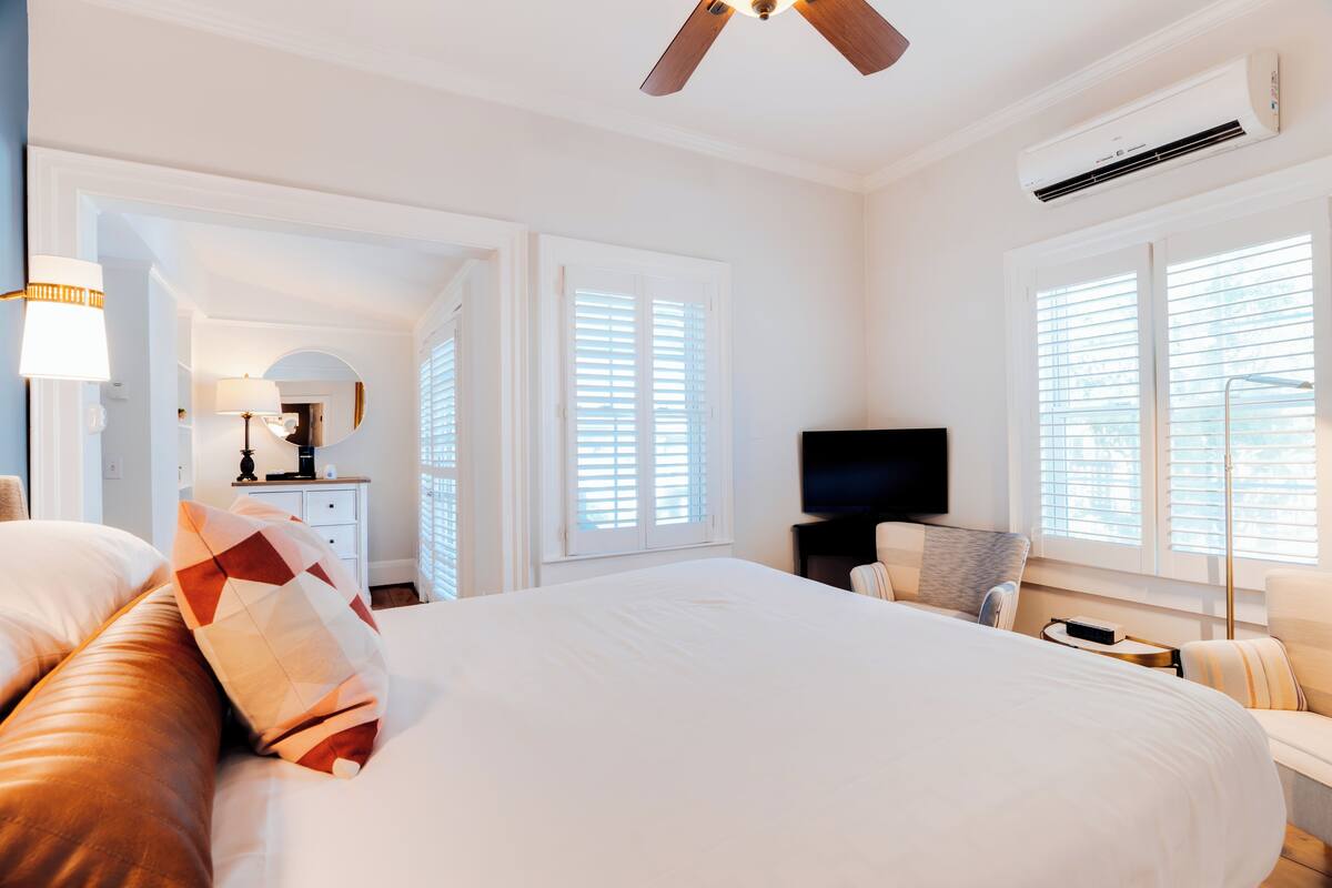 Une chambre spacieuse avec un grand lit, un ventilateur de plafond, une télévision et une table de chevet.