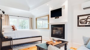 A modern bedroom with a large bed, a fireplace, a TV mounted above it, and a window with curtains.