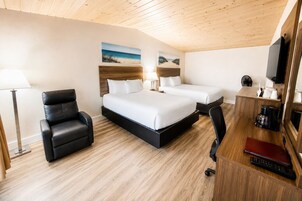 Habitación de hotel con dos camas, un escritorio con computadora, una silla, una lámpara y un televisor.