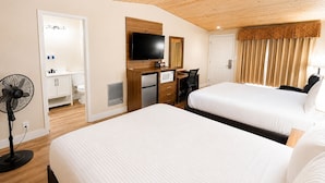 Habitación de hotel con dos camas, un escritorio, un televisor, un ventilador y un baño.