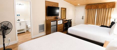 A hotel room with two beds, a desk, a TV, a fan, and a bathroom.