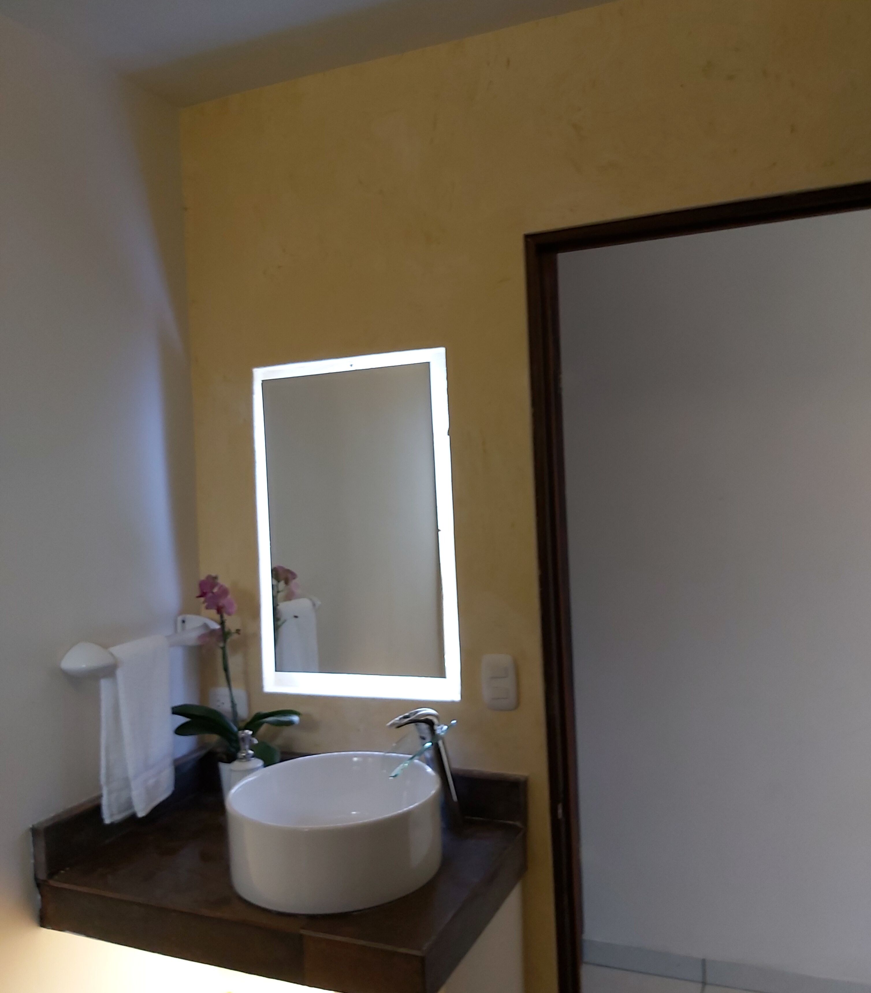 Un baño con lavamanos blanco, un espejo y un perchero para toallas.