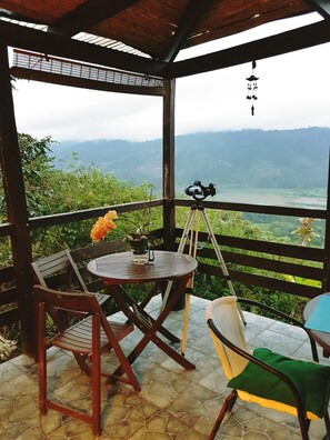 A covered outdoor seating area with a table and chairs, a telescope, and a view of a mountainous landscape.
