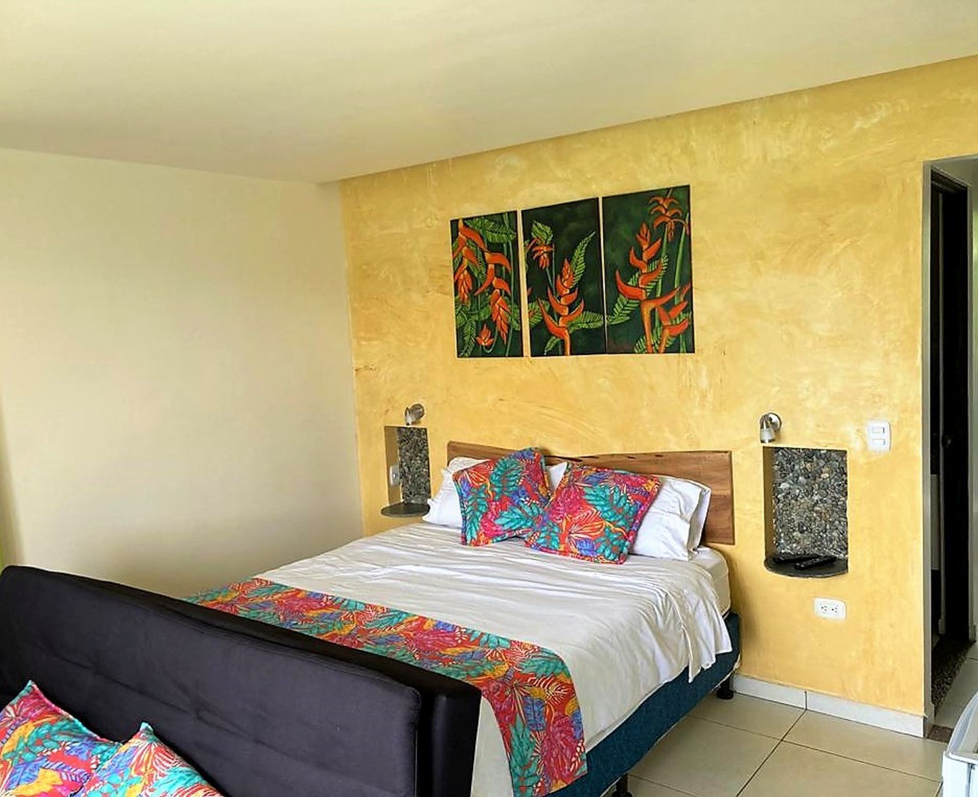 Un dormitorio con cama, mesita de noche y estante en la pared.