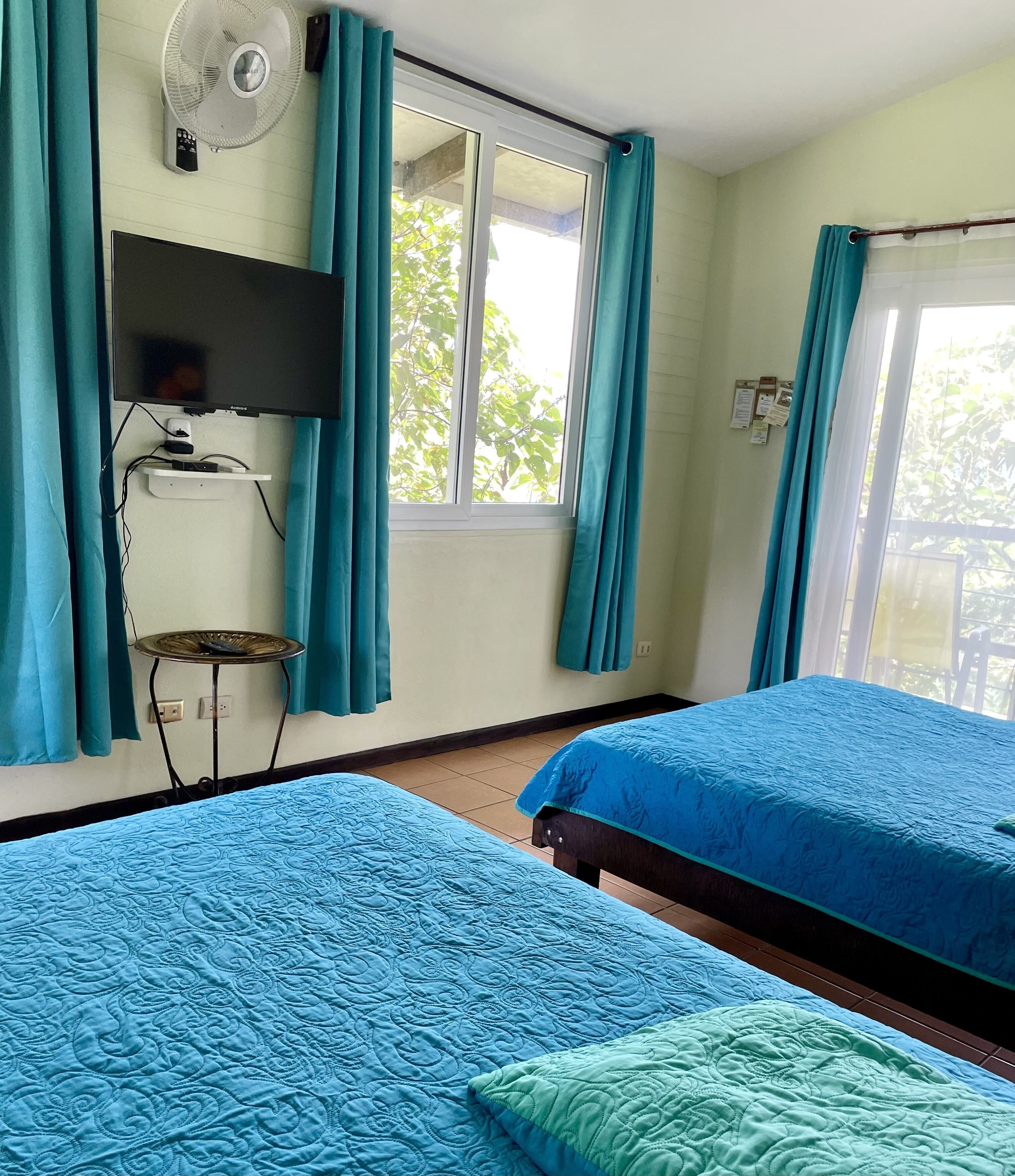 Een kamer met twee bedden, een televisie, een ventilator en een raam met gordijnen.