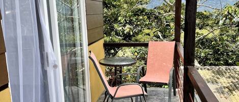 A balcony with a table and chairs, a blue mat, and a view of greenery and mountains.